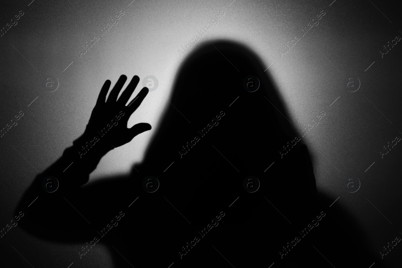 Photo of Silhouette of ghost behind glass against light grey background