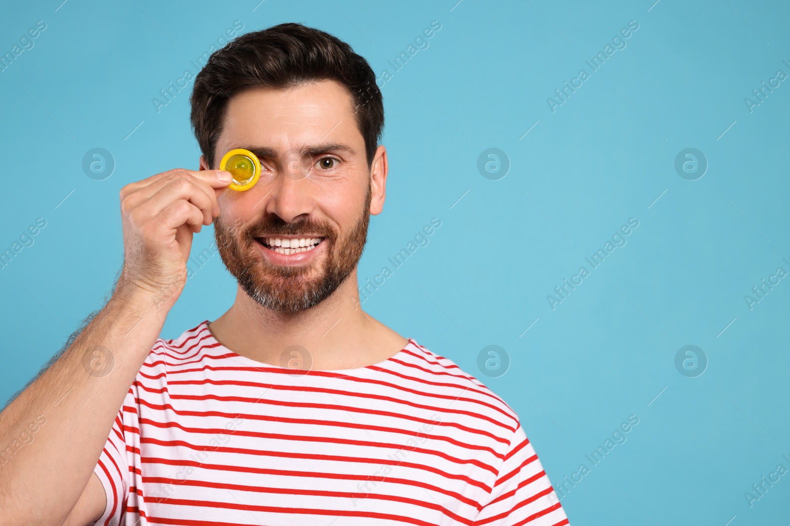 Photo of Happy man holding condom on light blue background, space for text. Safe sex