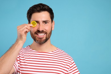 Happy man holding condom on light blue background, space for text. Safe sex
