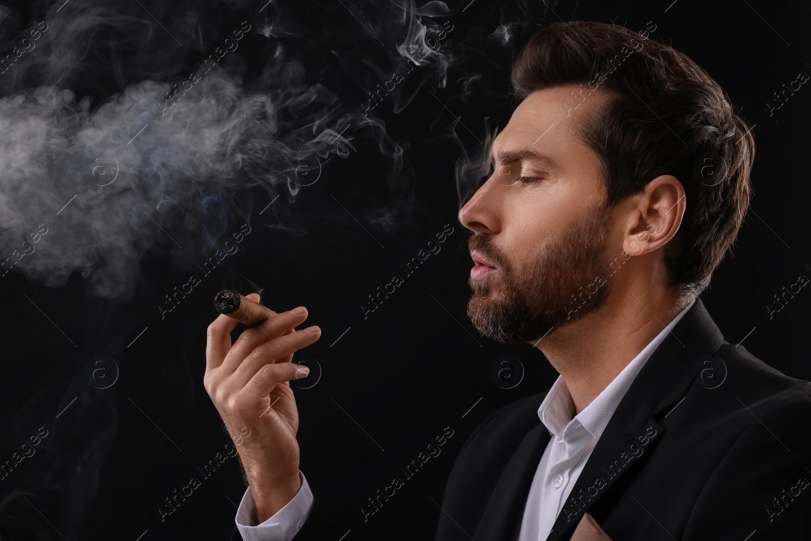 Photo of Handsome man smoking cigar on black background. Space for text