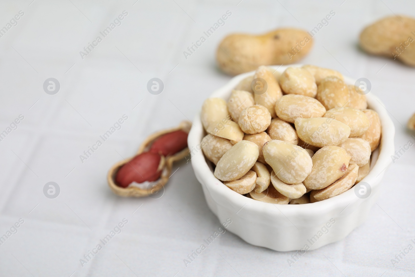 Photo of Fresh peeled peanuts in bowl on white tiled table, closeup. Space for text