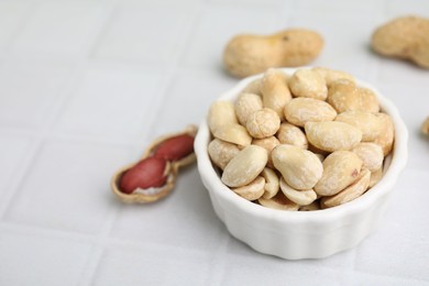 Fresh peeled peanuts in bowl on white tiled table, closeup. Space for text