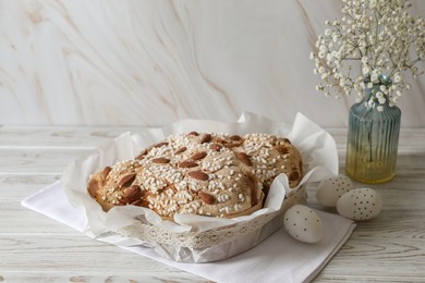 Photo of Delicious Italian Easter dove cake (traditional Colomba di Pasqua), decorated eggs and flowers on white wooden table. Space for text