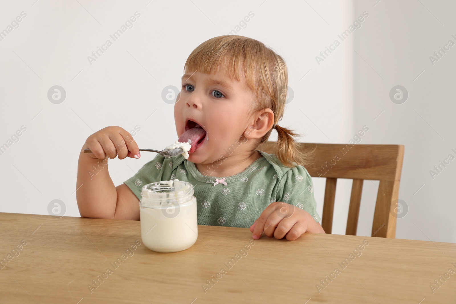 Photo of Cute little child eating tasty yogurt with spoon at wooden table indoors