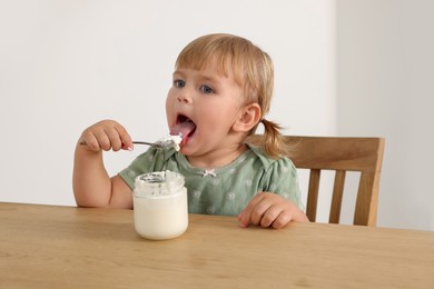 Cute little child eating tasty yogurt with spoon at wooden table indoors