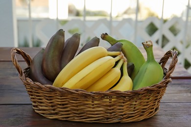 Photo of Wicker basket with different sorts of bananas on wooden table