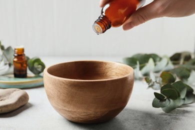 Photo of Woman dripping eucalyptus essential oil from bottle into bowl at light grey table, closeup