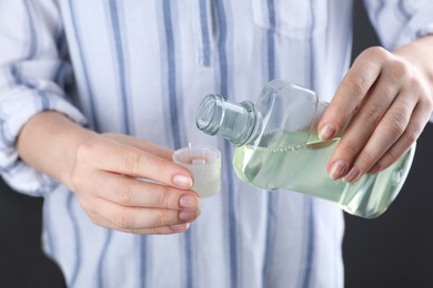 Photo of Woman pouring mouthwash from bottle into lid, closeup