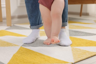 Photo of Mother supporting her baby son while he learning to walk on carpet at home, closeup