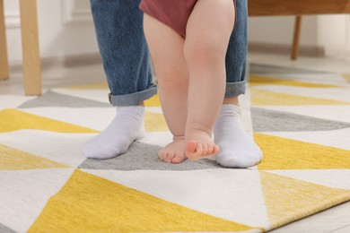 Mother supporting her baby son while he learning to walk on carpet at home, closeup