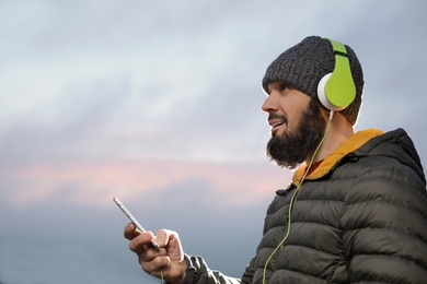 Photo of Mature man with headphones listening to music outdoors, space for text