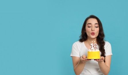 Coming of age party - 18th birthday. Woman blowing number shaped candles on cake against light blue background, space for text