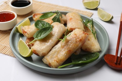 Photo of Plate with tasty fried spring rolls, spinach, arugula and lime on white table, closeup
