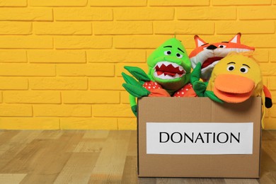 Photo of Donation box with different soft toys on floor near yellow brick wall, space for text