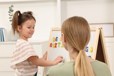 Photo of Mom teaching her daughter alphabet with magnetic letters at home