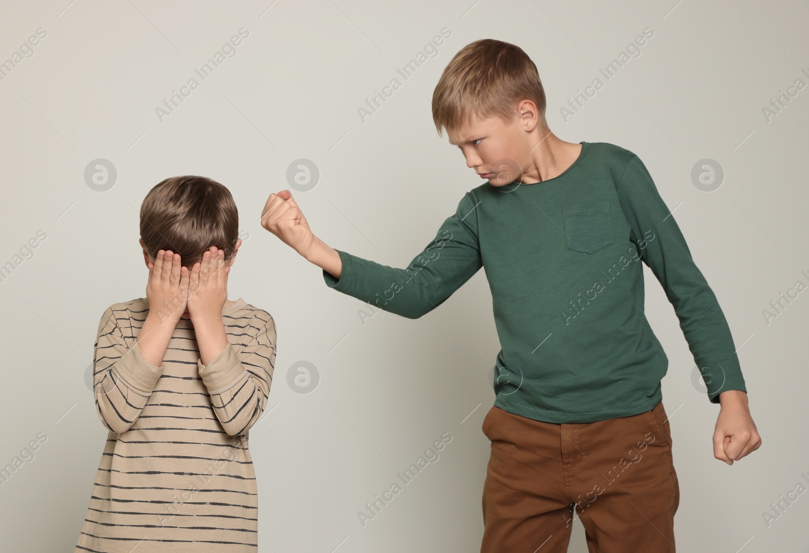 Photo of Boy with clenched fist looking at scared kid on light grey background. Children's bullying