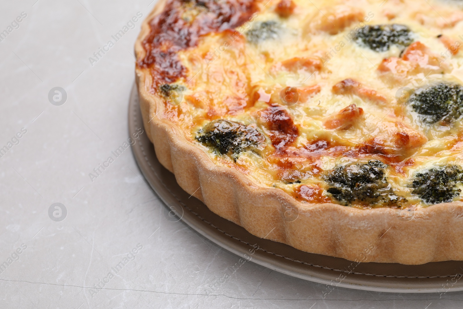 Photo of Delicious homemade quiche with salmon and broccoli on light gray table, closeup. Space for text