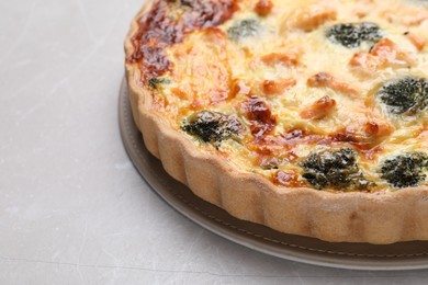 Delicious homemade quiche with salmon and broccoli on light gray table, closeup. Space for text