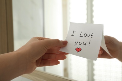 Woman putting sticky note with text I love you! on mirror, closeup