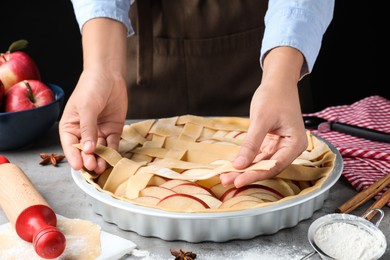 Photo of Woman decorating raw apple pie at grey table, closeup