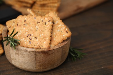 Photo of Cereal crackers with flax, sesame seeds and rosemary in bowl on wooden table, closeup. Space for text