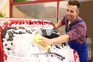 Photo of Male worker cleaning vehicle with sponge at car wash