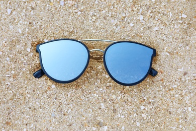 Stylish sunglasses on sandy beach, top view