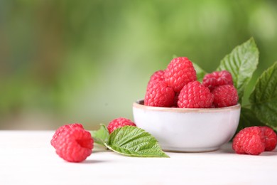 Photo of Tasty ripe raspberries and green leaves on white table outdoors. Space for text