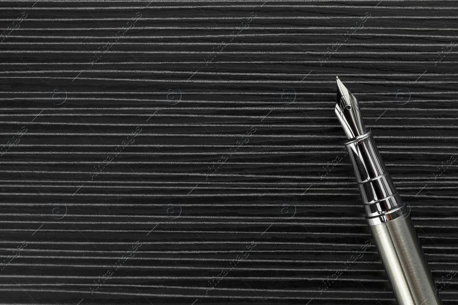 Photo of Stylish silver fountain pen on black wooden table, top view. Space for text