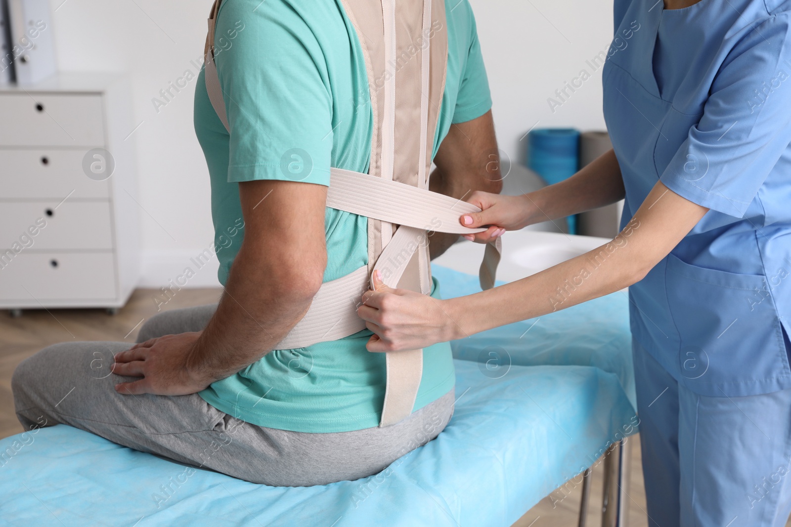 Photo of Orthopedist helping patient to put on posture corrector in clinic, closeup. Scoliosis treatment