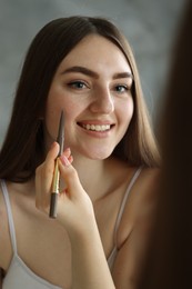 Photo of Smiling woman drawing freckles with pen indoors