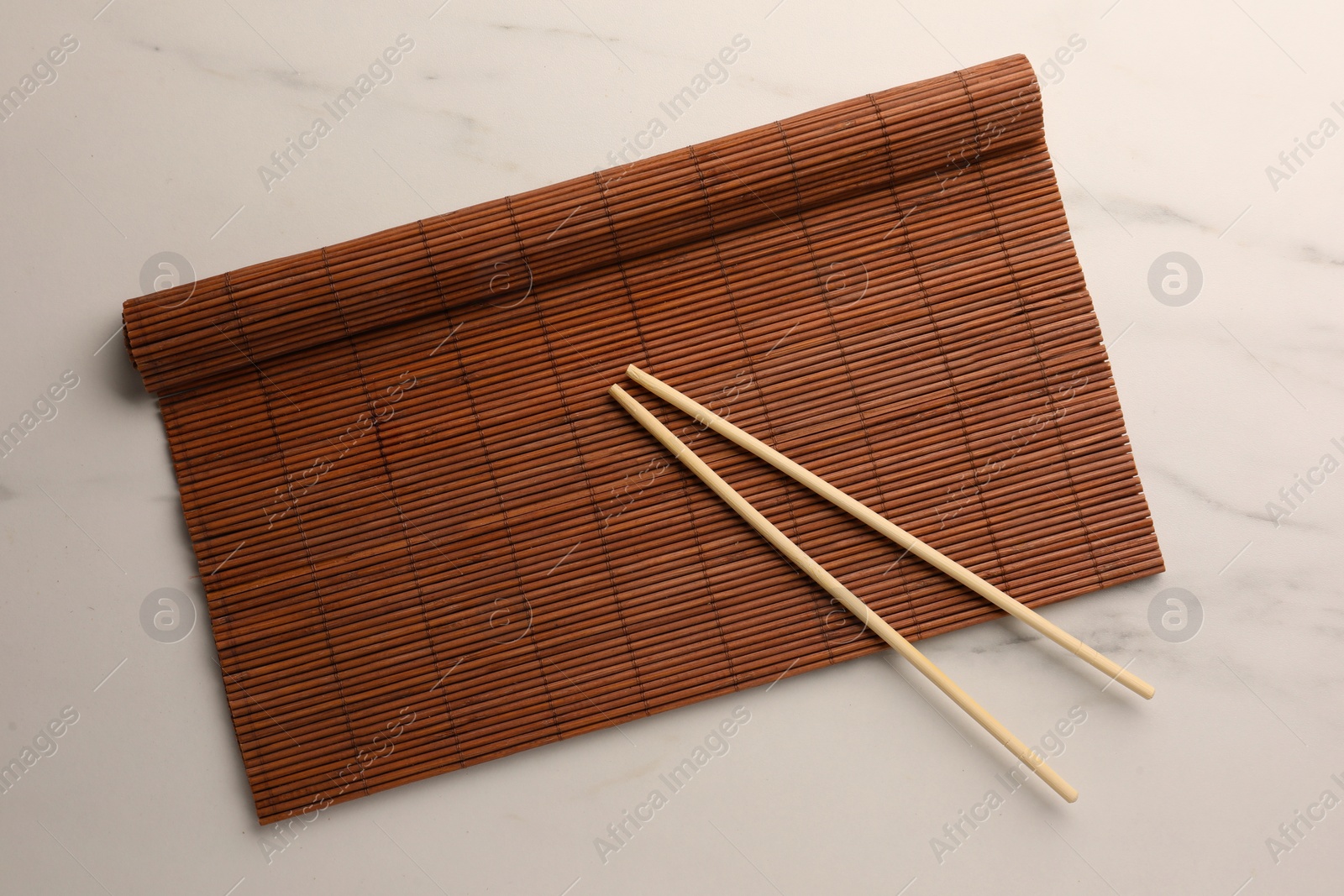 Photo of Rolled bamboo mat and chopsticks on white marble table, top view