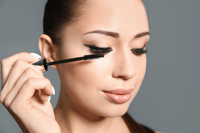Photo of Beautiful woman applying mascara on light grey background, closeup. Stylish makeup