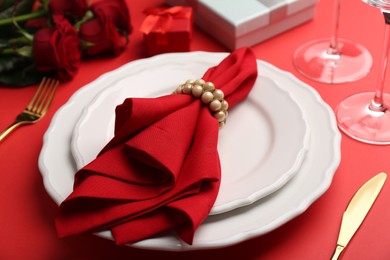 Photo of Place setting with gift boxes and bouquet of roses on red table, closeup. Romantic dinner