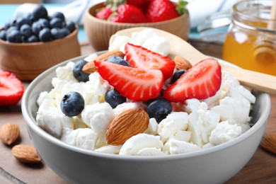 Photo of Bowl of fresh cottage cheese, berries and almonds on wooden board, closeup