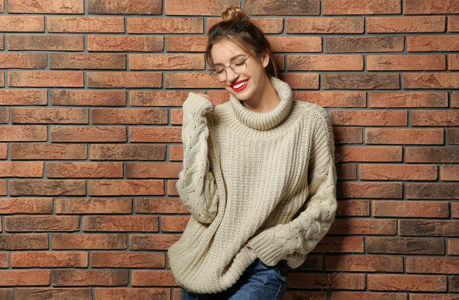 Photo of Beautiful young woman in warm sweater near brick wall