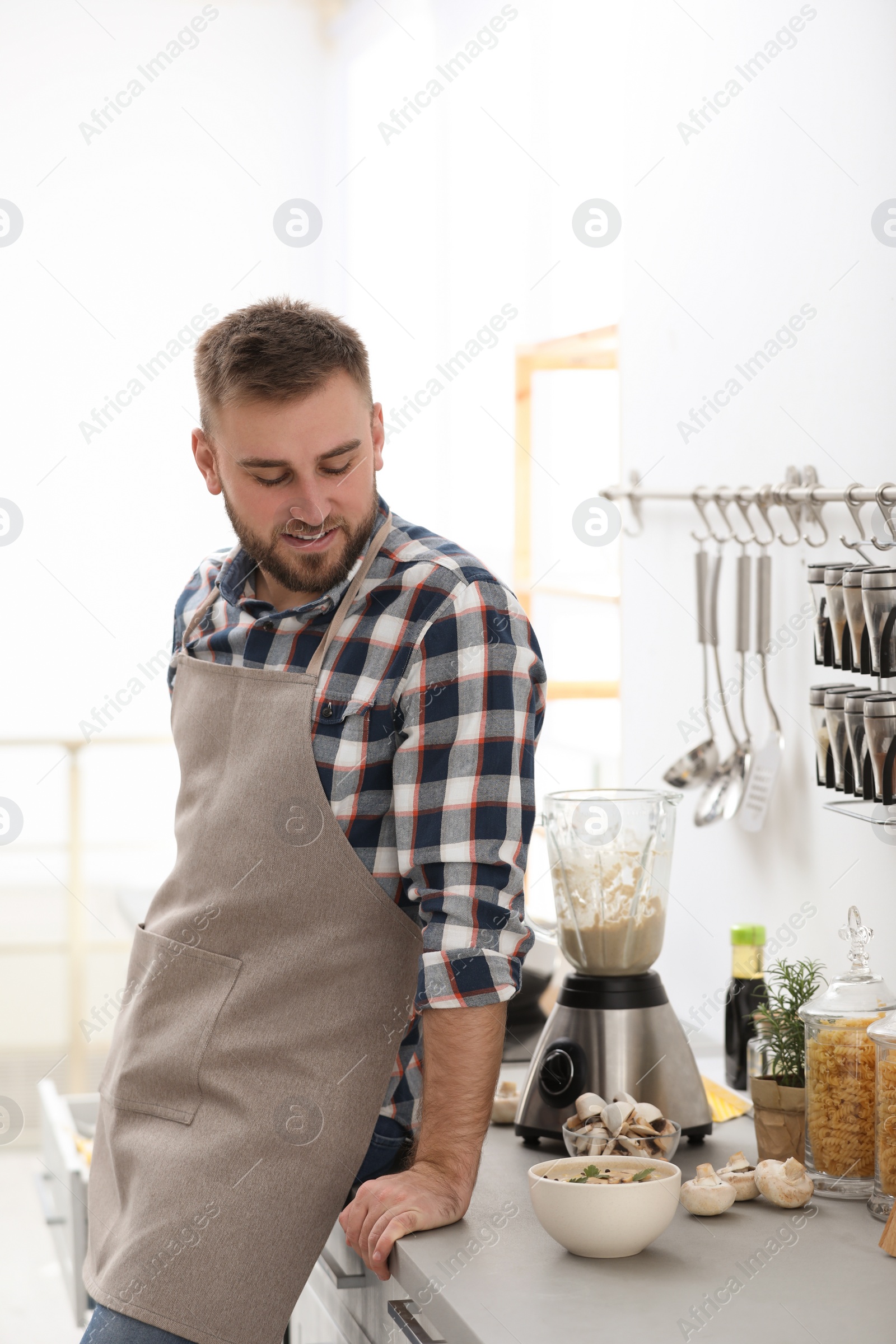 Photo of Young man with bowl of tasty cream soup in kitchen