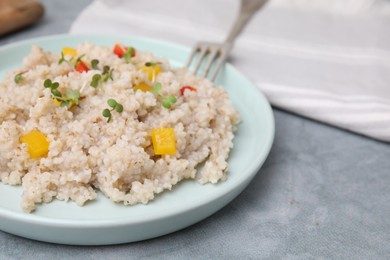 Photo of Delicious barley porridge with vegetables and microgreens on gray table, closeup
