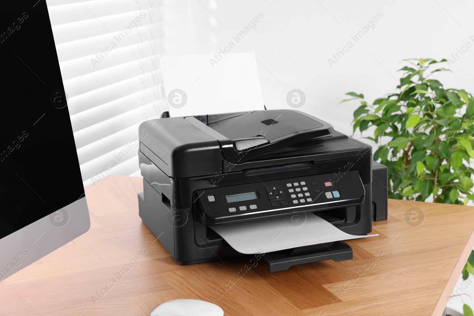 Photo of Modern printer with paper near computer on wooden table in home office