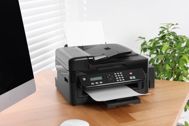 Modern printer with paper near computer on wooden table in home office