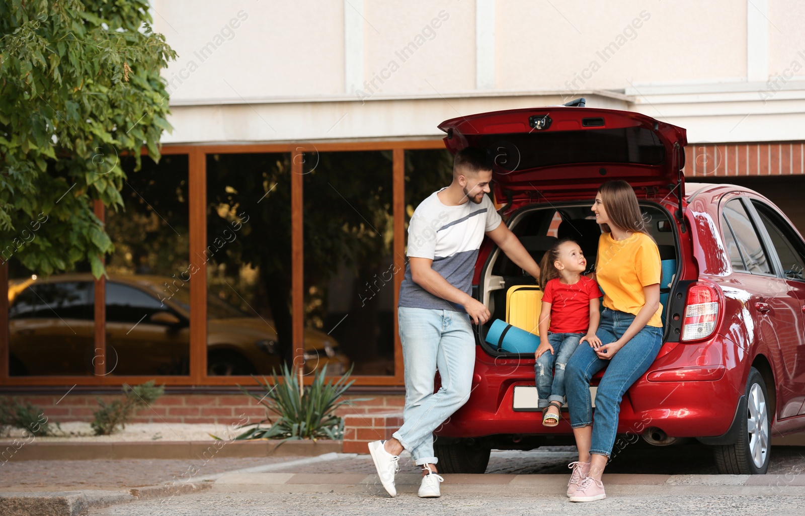 Photo of Happy family near car with open trunk on street