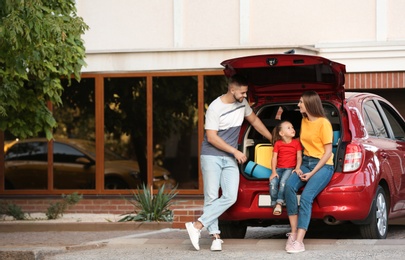 Photo of Happy family near car with open trunk on street