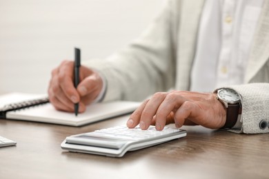 Professional accountant using calculator at wooden desk, closeup