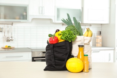 Photo of Textile shopping bags full of vegetables with fruits and juice on table in kitchen