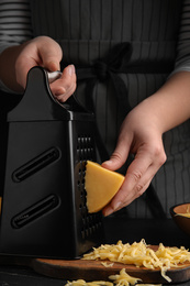 Woman grating fresh cheese at black table, closeup