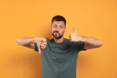 Photo of Man showing thumbs up and down on orange background