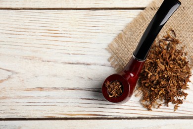 Photo of Smoking pipe, dry tobacco and sackcloth on white wooden table, top view. Space for text