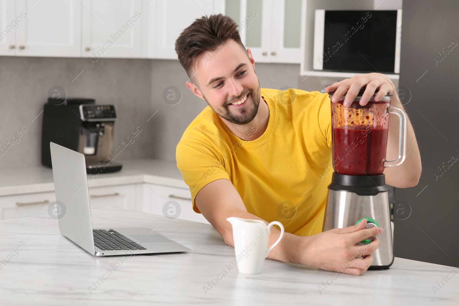 Photo of Happy man making smoothie while watching cooking online course in kitchen. Time for hobby