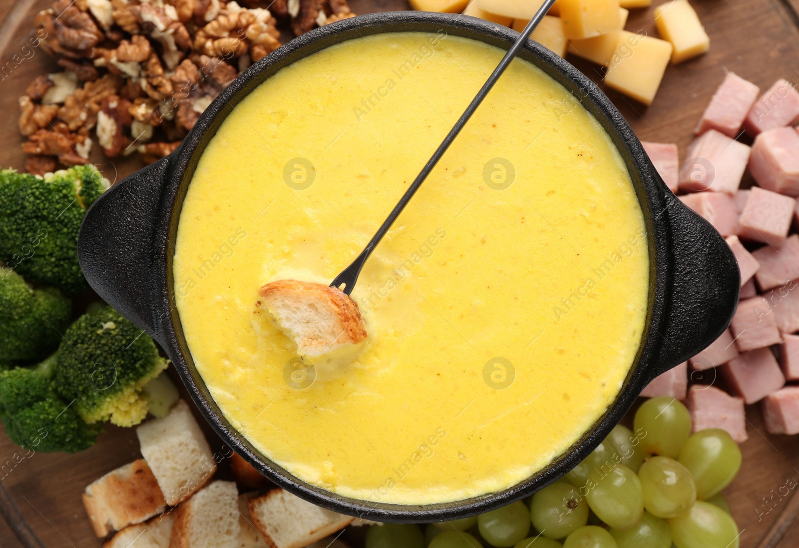 Photo of Fondue with tasty melted cheese, fork and different products on table, top view