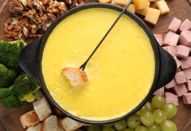Photo of Fondue with tasty melted cheese, fork and different products on table, top view